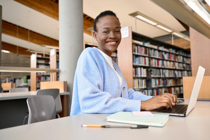 Dissertation student sitting in library with laptop