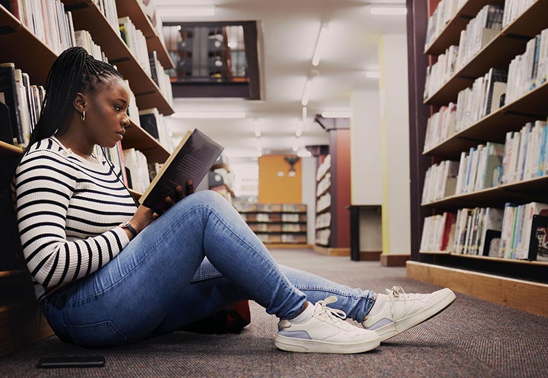Dissertation student studying literature, sitting on the floor of a library