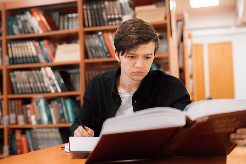 Student conducting a systematic literature review with books in the library